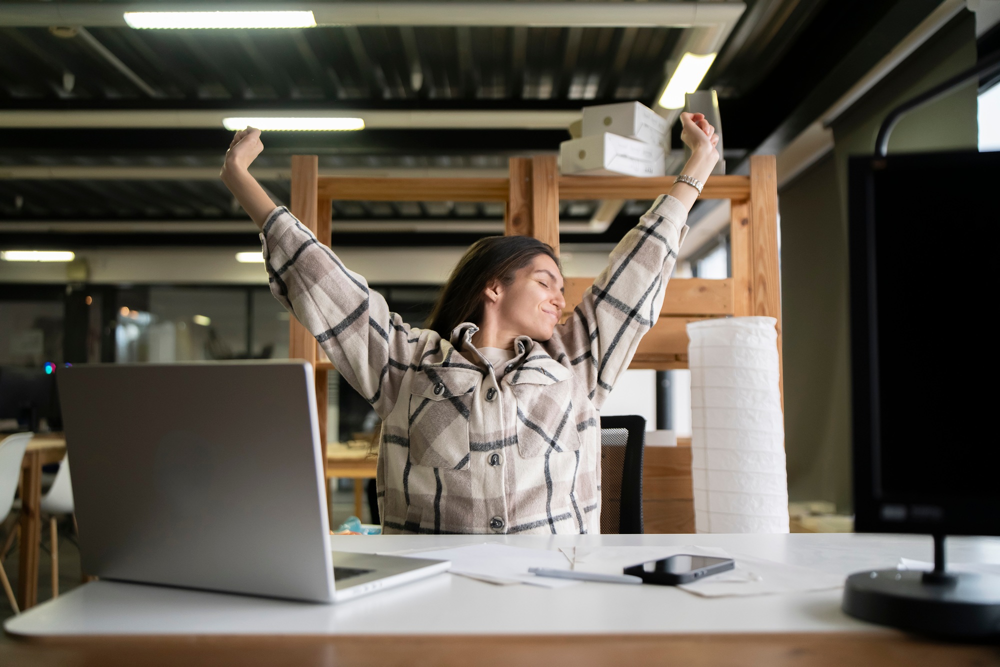 Woman Stretching Arms Upward During a Break in a Modern Office Workspace