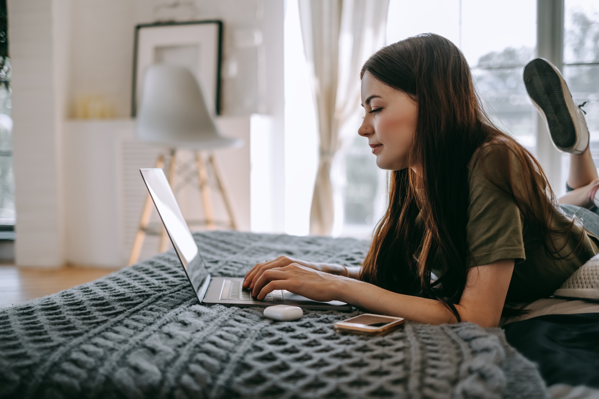 Attractive young caucasian woman working with laptop computer, lying on a bed at home