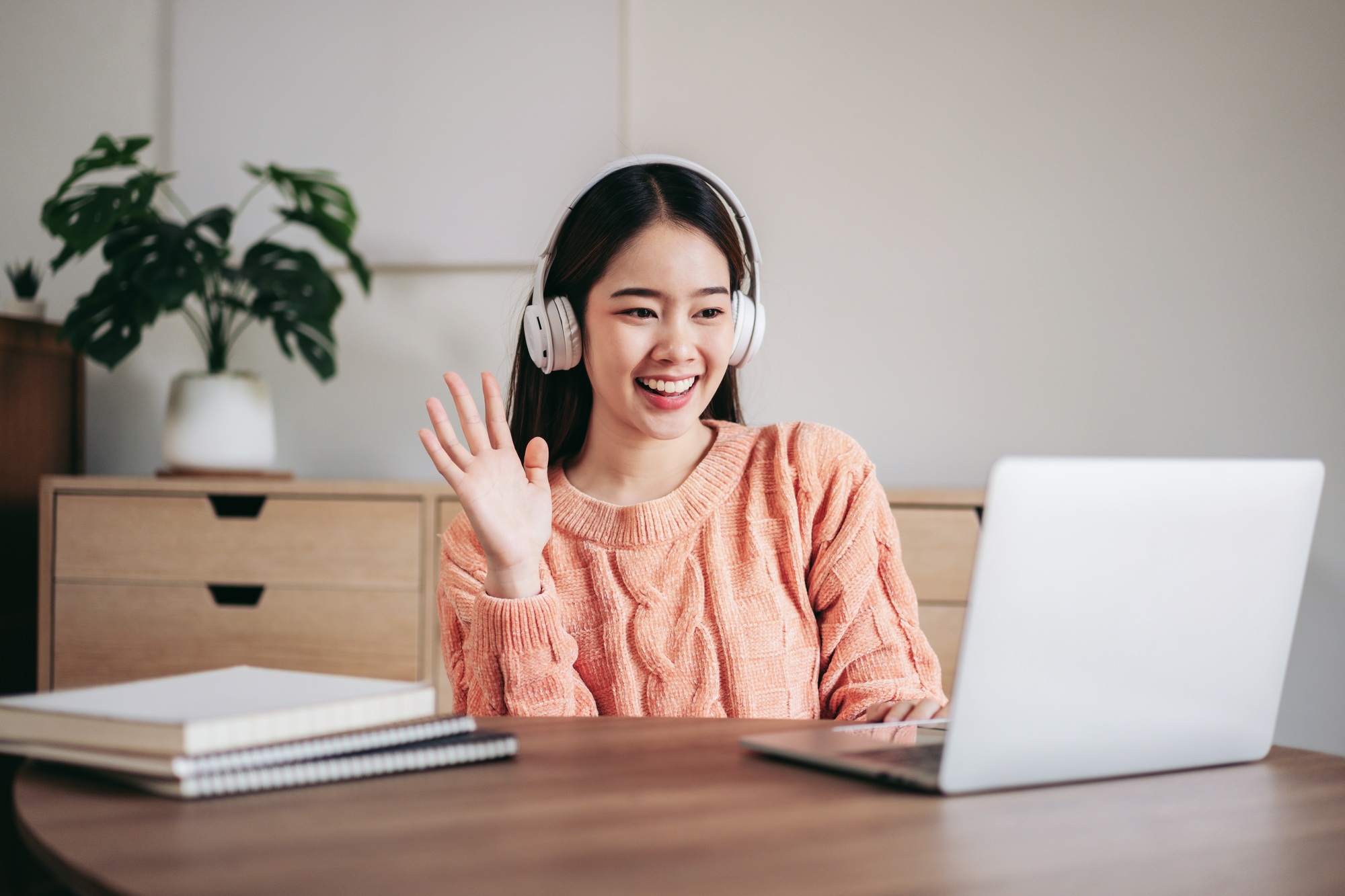 A woman wearing headphones is smiling and waving at the camera