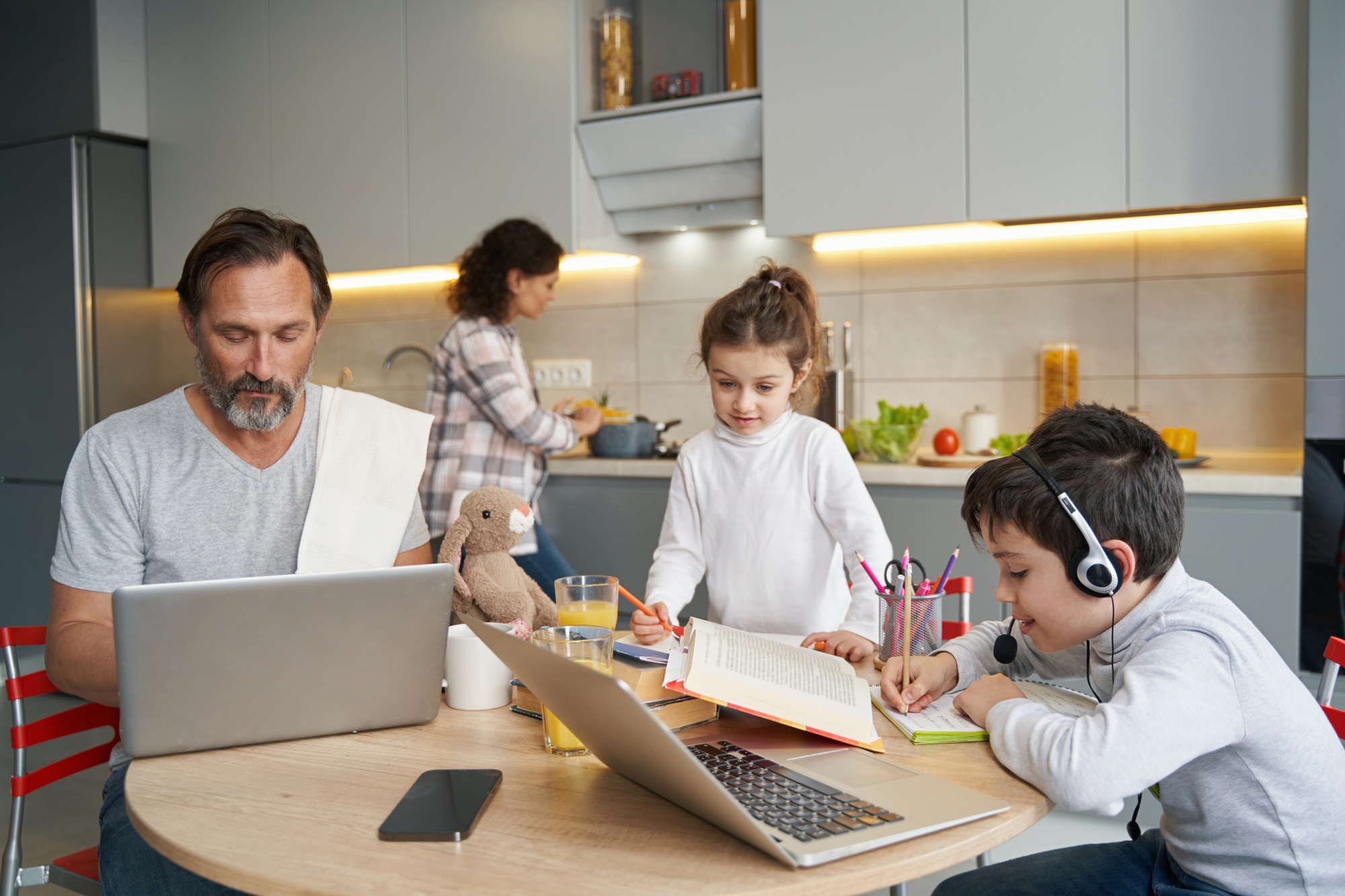 Family in kitchen working with homework and laptop at table