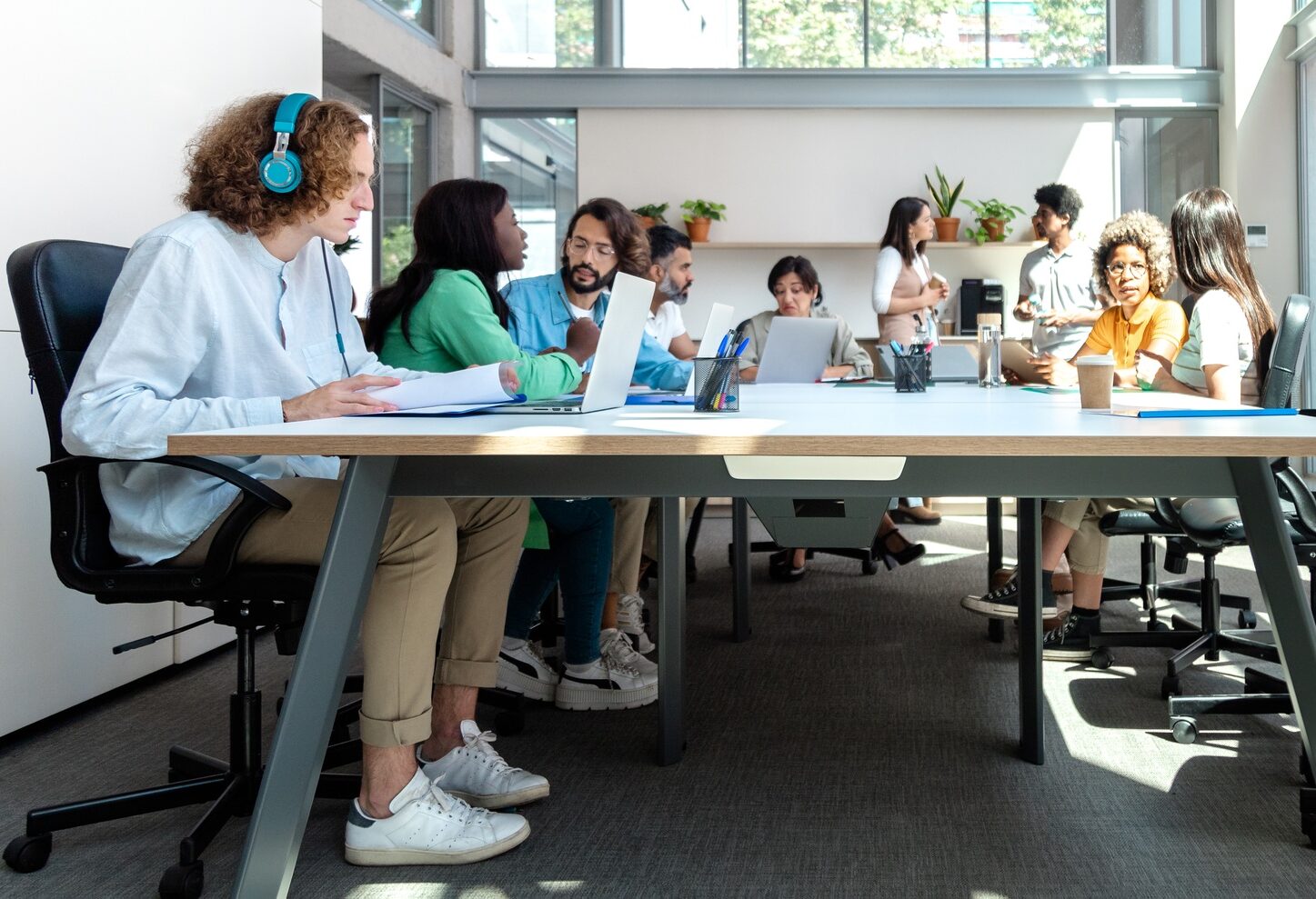 Spacious, luminous, busy office. Multiracial group of coworkers share big table in coworking space.